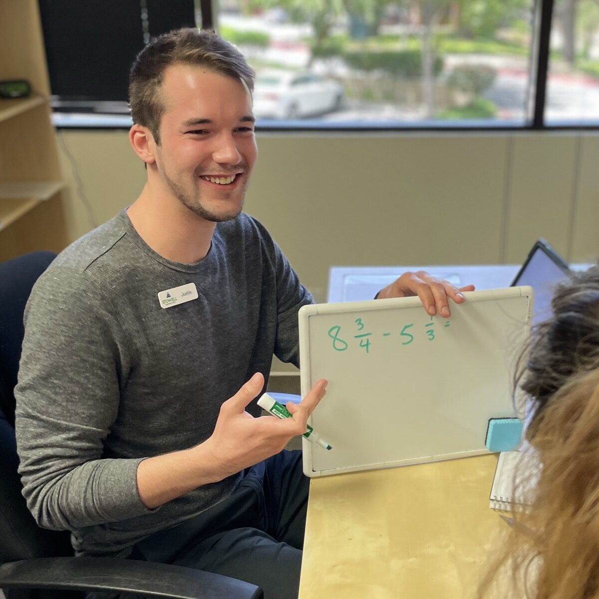 Smiling clinician working one-on-one with a student on a whiteboard during an attention and learning session at Stowell Learning Center